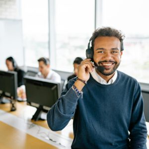 Cheerful male call center agent with headset in a bright office environment.