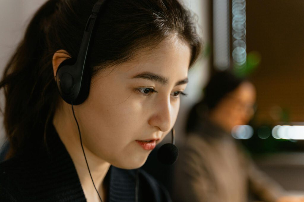 Focused Asian woman in headset providing customer support in office setting.