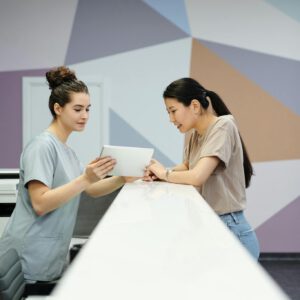 Two women interacting with a tablet at a modern reception desk indoors.